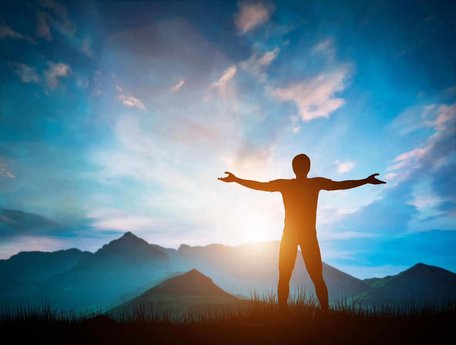 Man standing with arms raised looking at wonderful mountains landscape at sunset